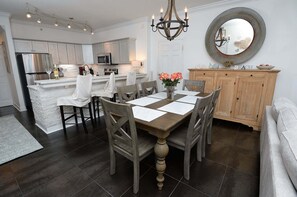 A modern kitchen with a central island, a dining area with a wooden table and chairs, and a large mirror above the island.