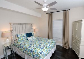 A bedroom with a bed, nightstands, a ceiling fan, a window with curtains, and a dresser.