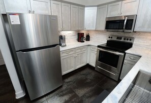 A modern kitchen with stainless steel appliances, white cabinetry, and a tiled backsplash.