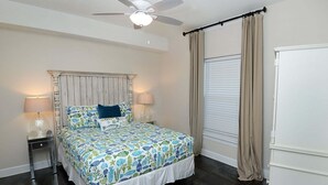 Ein Schlafzimmer mit einem Bett, zwei Nachttischlampen, einem Deckenventilator, einem Fenster mit Vorhängen und einer weißen Kommode.