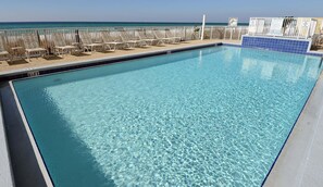 A clear swimming pool with lounge chairs and a view of the ocean.