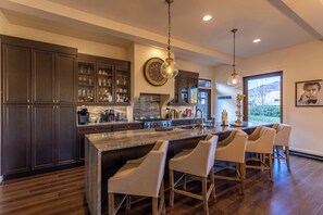 A kitchen with dark cabinets, a marble island, and bar stools. - Maynard Rocks IV at Elk Creek (Banner Elk)