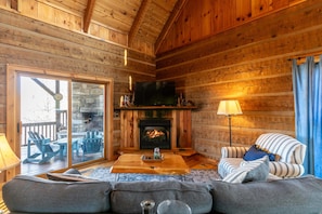 A log cabin interior with a fireplace, a sofa, a coffee table, and a television. - Walk In The Clouds (Boone)