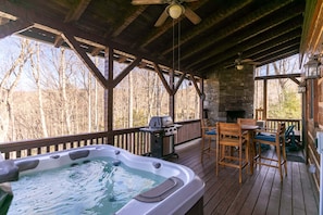 Een houten terras met een jacuzzi, een barbecue en een tafel met stoelen.