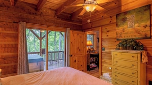 Ein Schlafzimmer einer Holzhütte mit einem Bett, einem Schminktisch, einem Deckenventilator und Blick ins Freie.