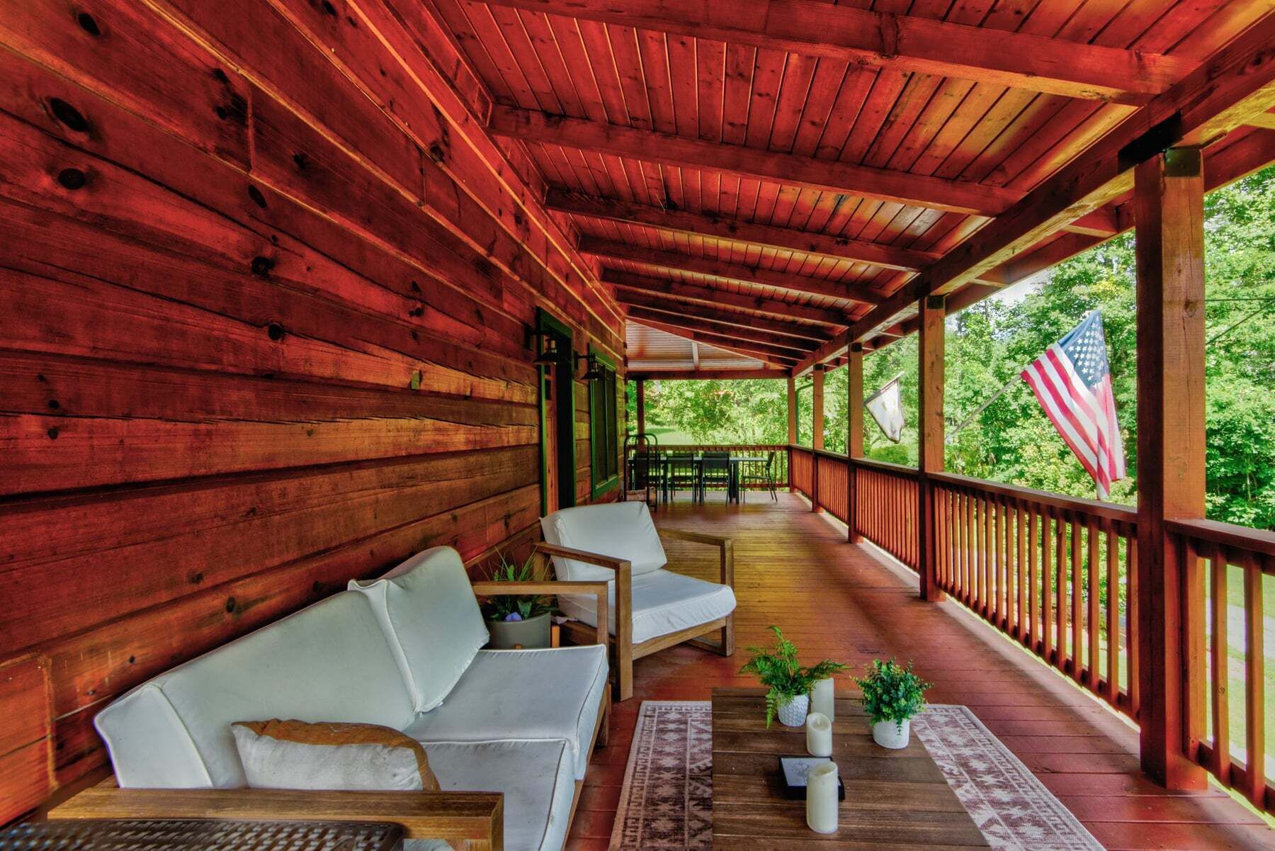 A covered porch with wooden walls, a white sofa, a table, and potted plants.