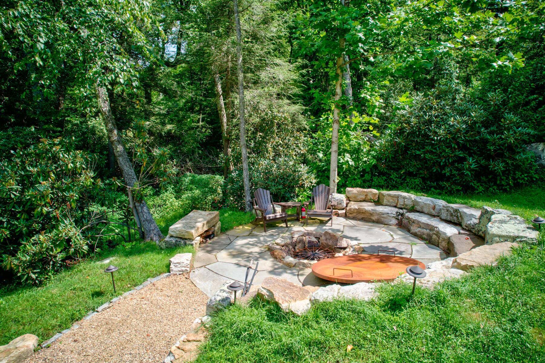 A circular stone fire pit with seating, surrounded by a stone wall and a gravel path.