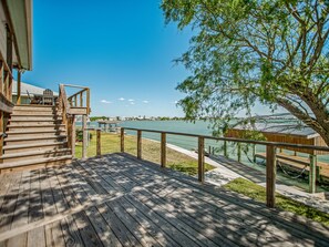 Une terrasse en bois avec une rambarde, un escalier et une vue sur un lac, avec des bâtiments visibles au loin.