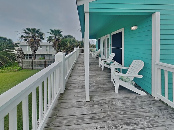 A wooden deck with white railings, a turquoise building, and several white Adirondack chairs. - Sundancers (Galveston)