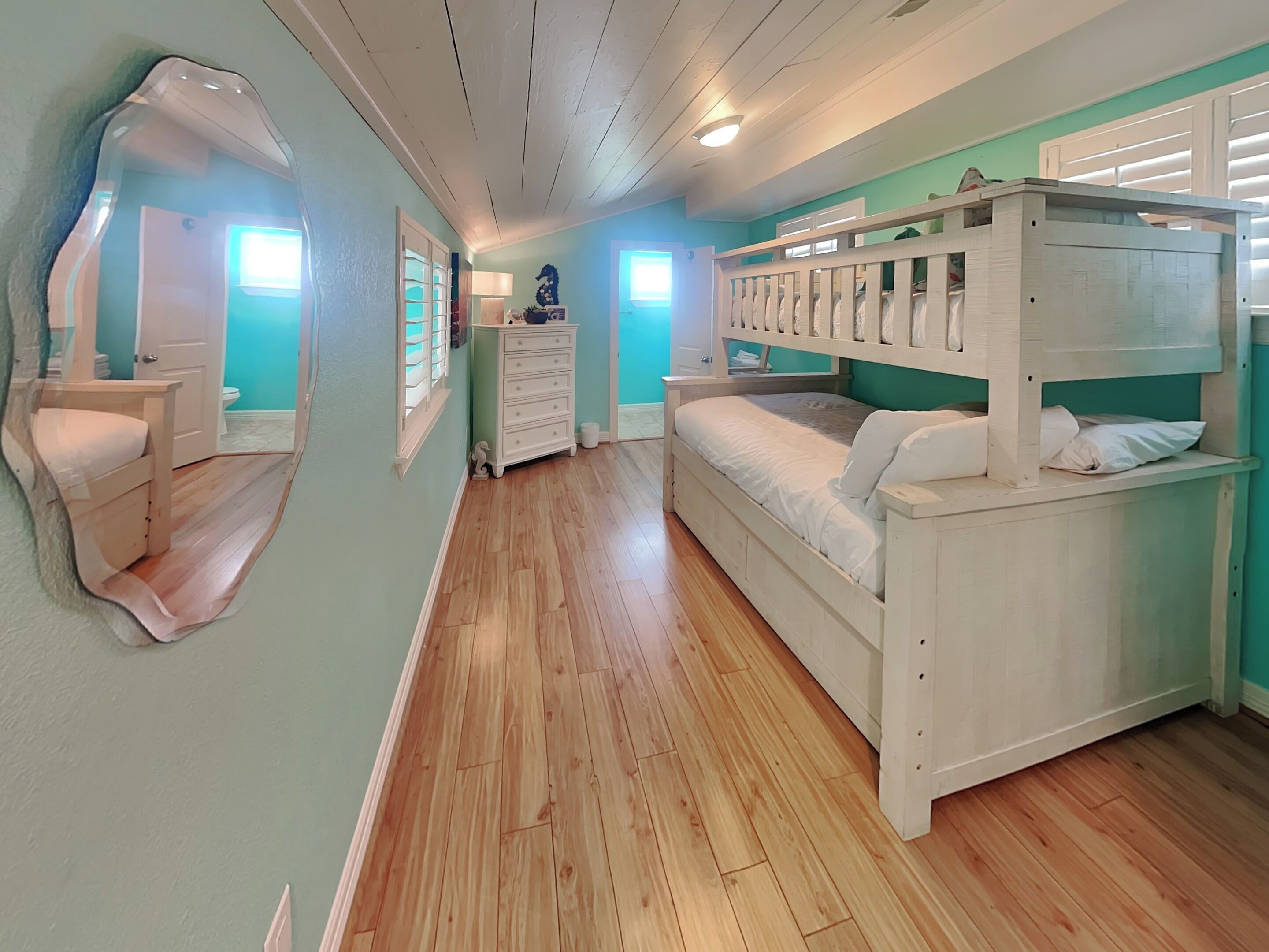 A bedroom with a bunk bed, a dresser, a mirror, and a window.
