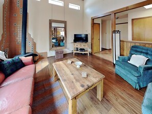 Ein Wohnzimmer mit Couchtisch aus Holz, einem blauen Sofa, einem rosafarbenen Sofa, einem Fernseher und einem Spiegel.