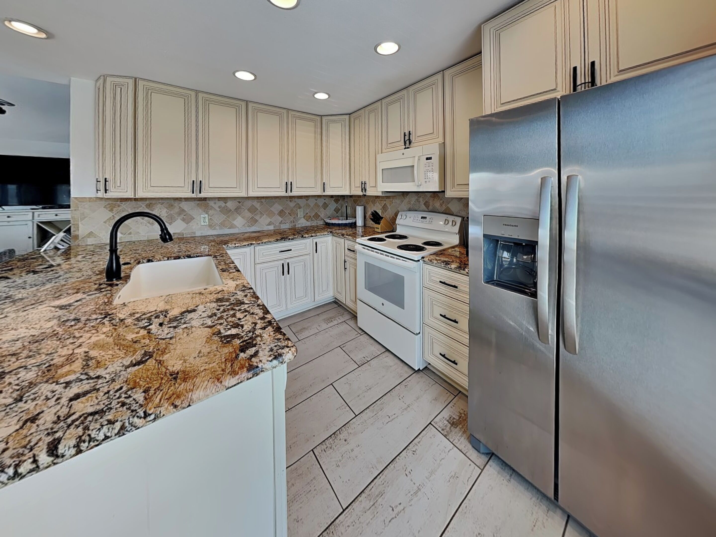 A modern kitchen with white cabinets, a granite countertop, a stainless steel refrigerator, a built-in oven, and a microwave.