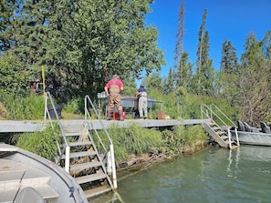 Eine Brücke mit Metallgeländern und Stufen, die über ein Gewässer führt, umgeben von Grünpflanzen und Bäumen.