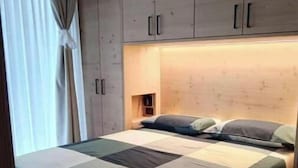 A bedroom with a wooden bed frame, a quilted mattress, and built-in wooden cabinets above the bed. - 3 - Bormio Apartments Al Pradais - First P. WEST (Bormio)