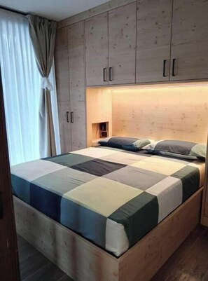 Ein Schlafzimmer mit einem Bettgestell aus Holz, einer gesteppten Matratze und eingebauten Holzschränken über dem Bett.