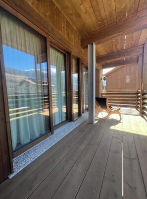 Eine Holzterrasse mit großen Schiebeglasfenstern, einer Holzbank und Blick auf die Landschaft.