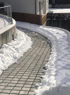 Ein verschneiter Außenbereich mit einem gepflasterten Weg und einer Holzbeschreibung.