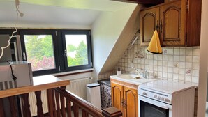 A kitchen with a window, a radiator, a sink, wooden cabinets, and a stove.