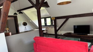 A loft-style living room with a red sofa, a television, and a dining area with a table and chairs.