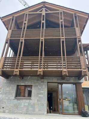 A multi-story building with a wooden balcony structure, stone facade, and a visible entrance. - 1 - Bormio Apartments Al Pradais - EAST Garden (Bormio)