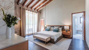 A bedroom with a bed, bedside tables, a bench, a vase with flowers, and a view of a hallway.