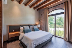 Ein Schlafzimmer mit einem großen Bett, einem Holzkopfteil, Nachttischen, einer Lampe und Blick durch ein großes Fenster.