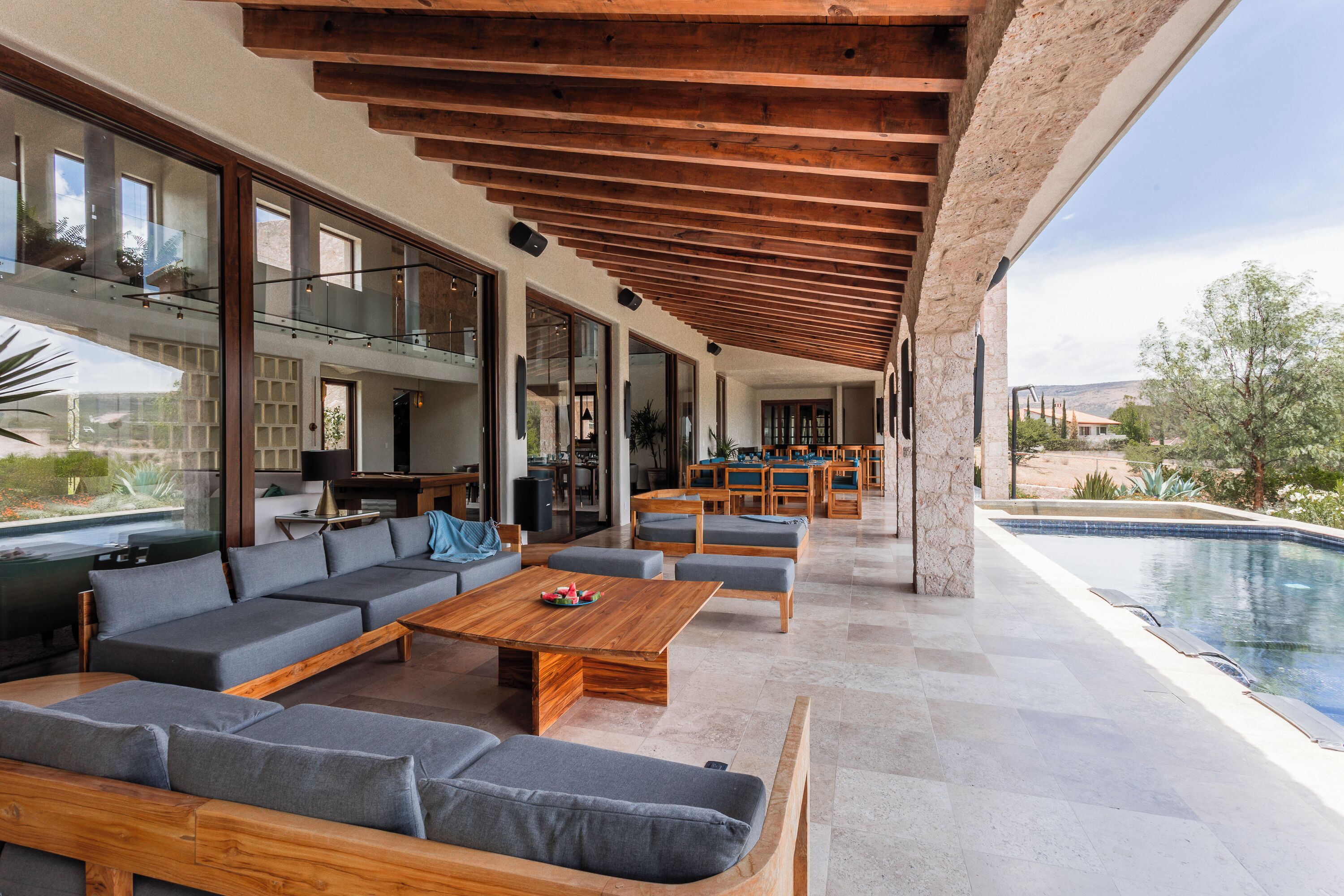 Un espacio exterior moderno con piscina, muebles de madera y una columna de piedra.