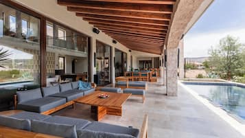 Un espacio exterior moderno con piscina, muebles de madera y una columna de piedra.