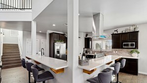 A modern kitchen with a central island, bar stools, dark cabinets, and a stainless steel refrigerator. - Modern Mountain Retreat in beautiful Ruidoso (Ruidoso)