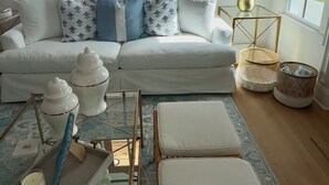 Uma sala de estar moderna com um sofá branco, almofadas estampadas, uma mesa de centro de vidro e vista para o exterior.