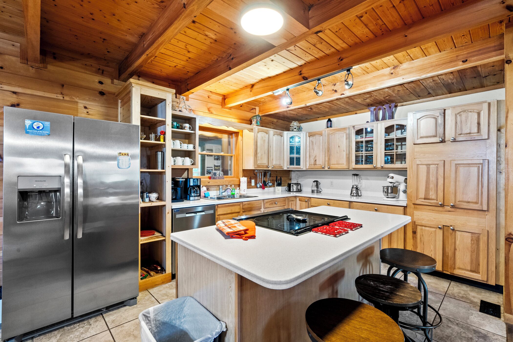 A modern kitchen with wooden cabinets, a stainless steel refrigerator, and a central island with stools.
