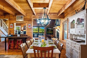 Ein Holzinterieur mit einem für sechs Personen gedeckten Esstisch, einer Bar und einer Küche mit weißen Schränken.