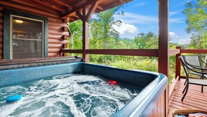 Ein Whirlpool auf einer Holzterrasse mit Blick auf eine bewaldete Landschaft.