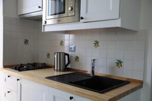 A kitchen with white cabinets, a stainless steel microwave, a gas stove, a sink, and decorative fruit tiles on the backsplash. - The little tower of Minuta - Allegro con Brio - retreat on the Amalfi Coast (Scala Costiera amalfitana)