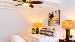Ein Schlafzimmer mit einem Bett, Deckenventilator, zwei Nachttischlampen, einem Nachttisch, einem gerahmten Bild und einem Teppich.