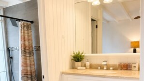 Ein Badezimmer mit Dusche, Toilette, Waschtisch mit Schubladen, einem Spiegel und einem Handtuchhalter.