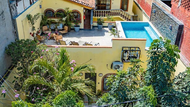 A yellow building with a tiled roof, a swimming pool, and outdoor seating. - Verde Suite - Zona Romantica Suites (Puerto Vallarta)