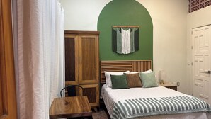 A bedroom with a bed, a wooden wardrobe, a chair, a desk, and a green wall. - Verde Suite - Zona Romantica Suites (Puerto Vallarta)