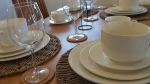 Una mesa de comedor dispuesta con platos, tazones y copas de vino blancos, sobre individuales tejidos.