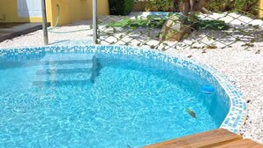Una piscina con cubierta de madera, rodeada por una zona de grava blanca y un edificio amarillo con tejado rojo.