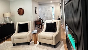 Een woonkamer met twee fauteuils, een salontafel, een televisie en een keuken op de achtergrond.