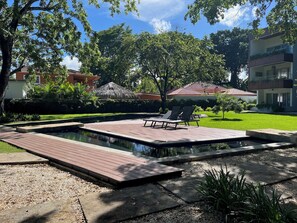 Ein Pool mit Holzterrasse, Liegestühlen und einer Rasenfläche mit Bäumen.