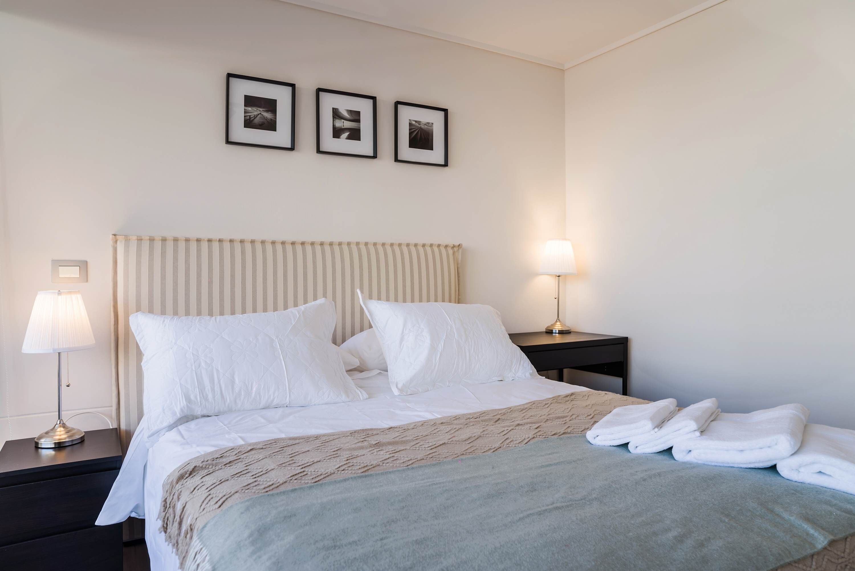 Une chambre d’hôtel avec un lit, deux lampes de chevet, une table de chevet et trois tableaux encadrés accrochés au mur.