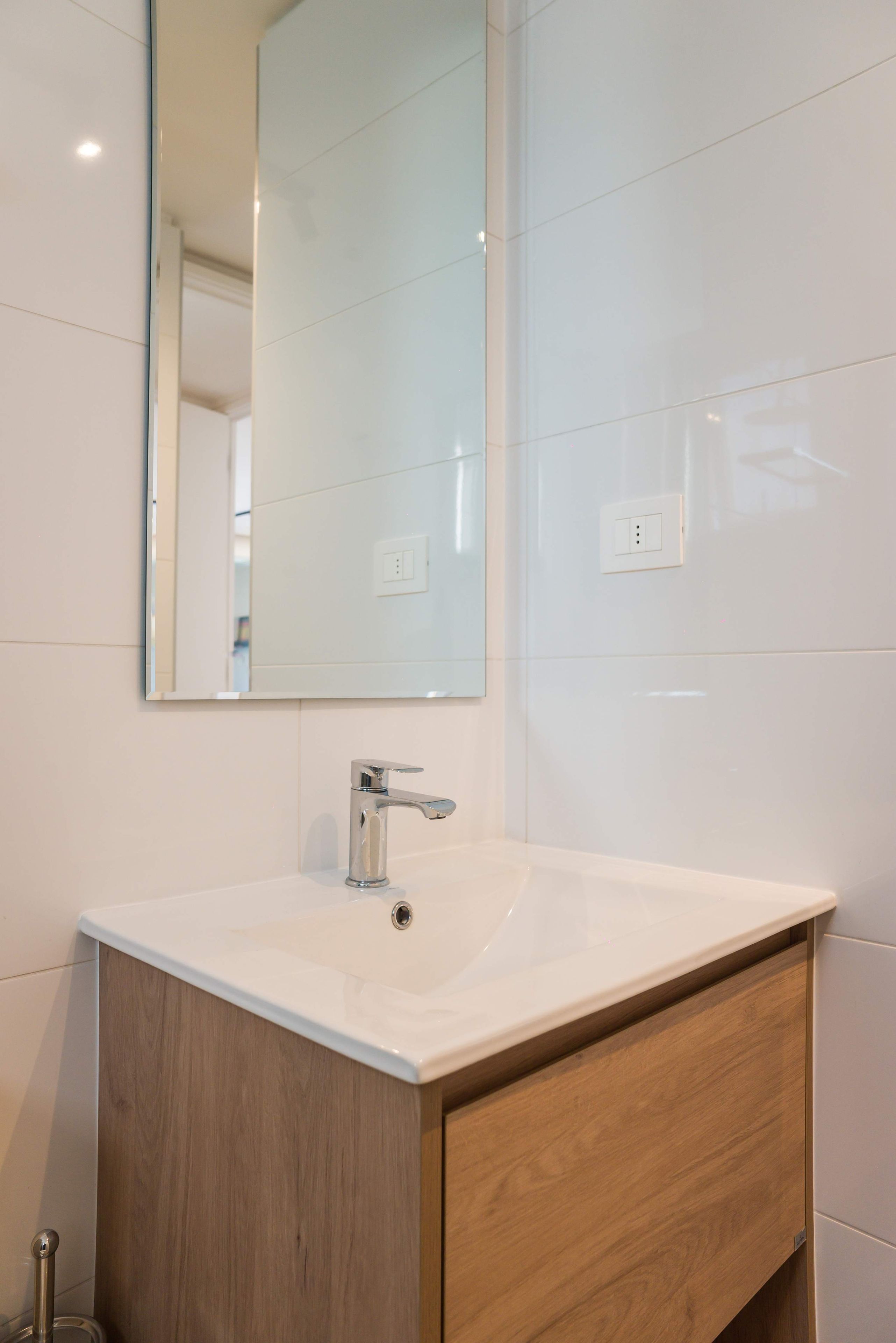 Un baño con un lavamanos blanco, un espejo y un mueble de madera.