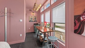 A pink-walled room with a wooden table, bar stools, a hanging light fixture, a painting, and a window with blinds. - Two Private Spaces | Downtown & Near Beach (Sheboygan)
