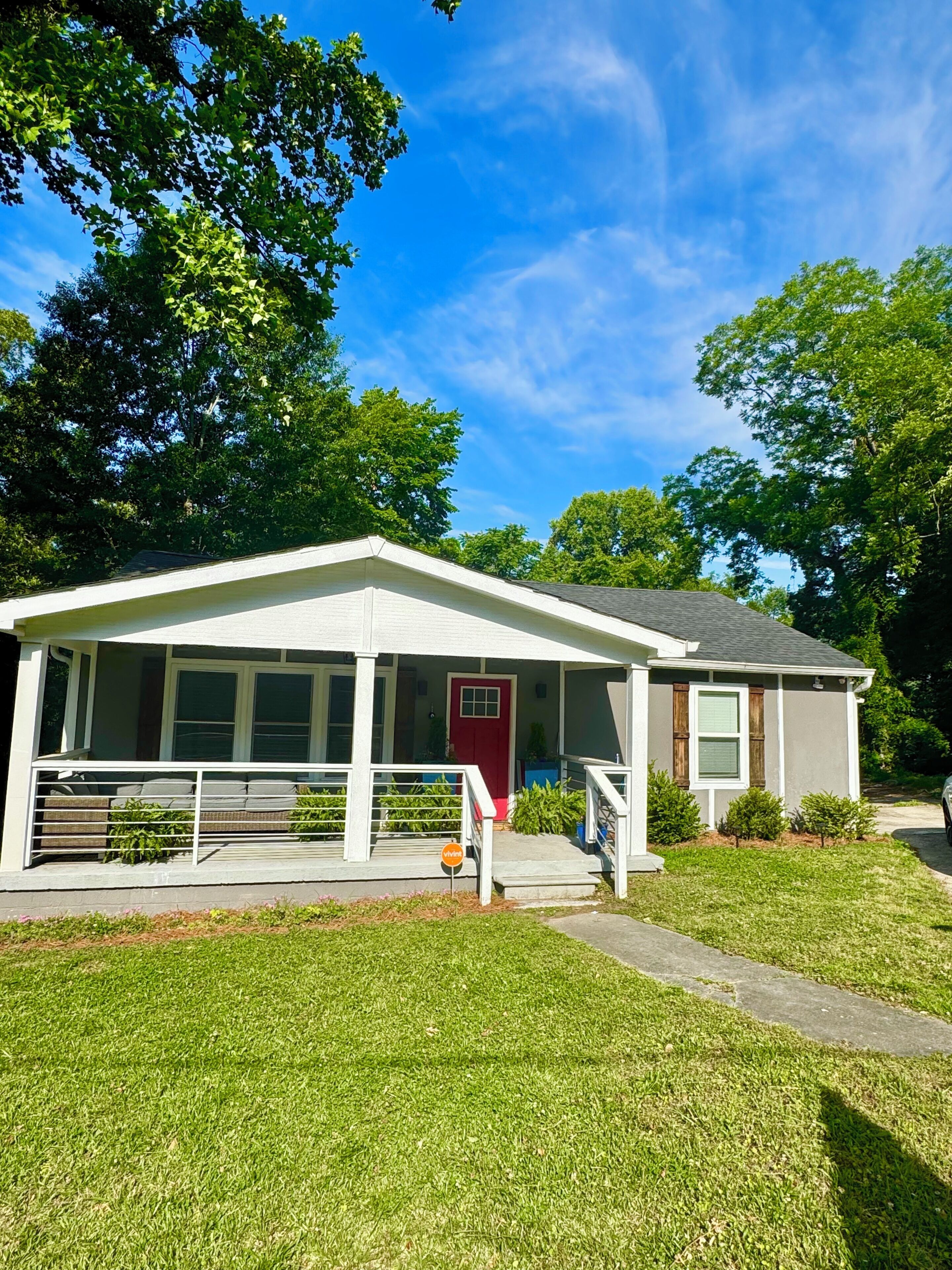 A single-story house with a porch, a red door, and a small front yard.