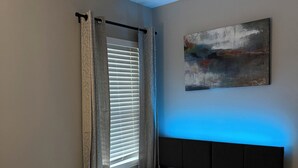 Un dormitorio con cama, ventana con persianas, un cuadro en la pared y cabecero.