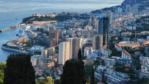Un paysage urbain côtier avec de hauts immeubles, une marina et une colline imposante en arrière-plan.