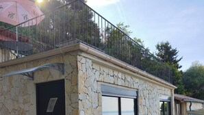 Un bâtiment en pierre avec une porte noire, un balcon doté d’une rambarde en métal et une vue sur la mer.