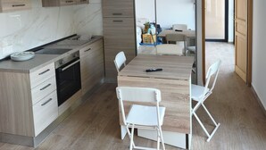 Et moderne køkken med indbygget ovn, spisebord med stole og udsigt til det tilstødende opholdsstue.